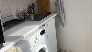 A compact kitchen with a washing machine, a wooden cutting board, and a towel hanging on the wall. - Cocoon Paris (Paris)
