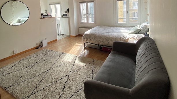 A spacious loft bedroom with exposed wooden beams, a large bed, a sofa, and a view of the city through the windows. - Cocoon Paris (Paris)