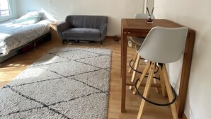 A room with a bed, a gray sofa, a wooden desk with a chair, and a patterned rug. - Cocoon Paris (Paris)