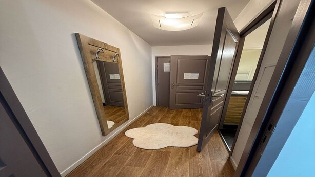 Un couloir avec un plancher en bois, un miroir et une porte sur laquelle est affichée une feuille de papier.