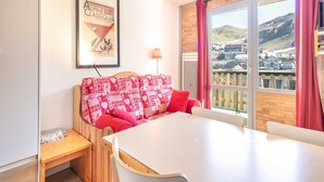A cozy room with a red patterned sofa, a white table, and a framed picture on the wall. - Studio in Chamrousse near Ski Resort (Chamrousse)