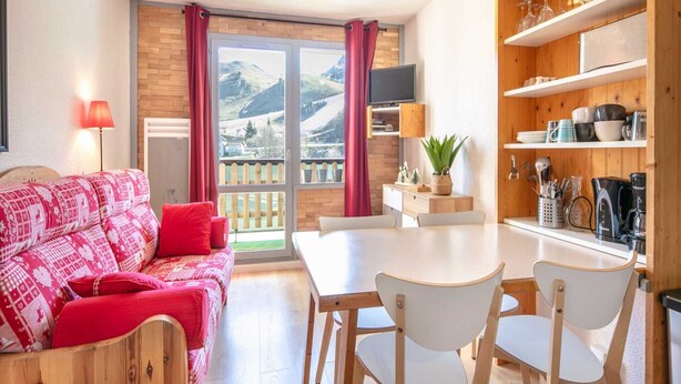 A cozy living room with a sofa, a dining table, and chairs. There is a kitchen area with shelves and a TV. - Studio in Chamrousse near Ski Resort (Chamrousse)