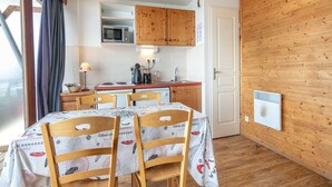 A compact kitchen with wooden cabinets, a microwave, and a coffee machine. There is a dining table with chairs covered in a patterned tablecloth. - Apartment in Chamrousse near Ski Slopes (Chamrousse)