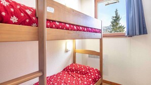 A bunk bed with red bedding, a window with a curtain, and a white wall. - Apartment in Chamrousse near Ski Slopes (Chamrousse)