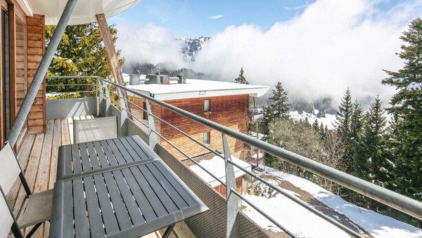 A balcony with a wooden table and chairs, overlooking a snowy landscape and a mountain in the distance. - Apartment in Chamrousse near Ski Slopes (Chamrousse)
