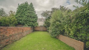 A backyard with a brick wall, a wooden fence, and a grassy lawn. - Modern 3BR Home with Stunning Garden | Banbury Stay (Banbury)