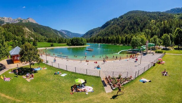 A lakeside resort with a swimming area, a small wooden cabin, and a grassy area with umbrellas. - Apartment in Allos near Ski Resort (Allos)