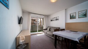 A modern living room with a sofa, a dining table, and a TV mounted on the wall. - Apartment in Allos near Ski Resort (Allos)