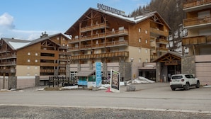A multi-story hotel with wooden balconies, a ski resort sign, and a snow-covered ground. - Apartment in Allos near Ski Resort (Allos)