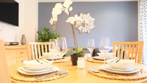 Une table à manger dressée avec de l’argenterie blanche, des couverts et des verres à vin, entourée de chaises.