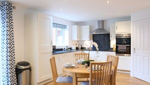 Une cuisine moderne avec des meubles blancs, un four en acier inoxydable et un coin repas comprenant une table ronde et des chaises.