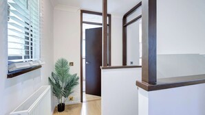 Un pasillo con un radiador, una planta en maceta y una puerta que da a otra habitación.
