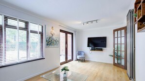 Un salón amplio con una mesa de centro de vidrio, un televisor de pantalla plana montado en la pared y un ventanal grande con persianas.