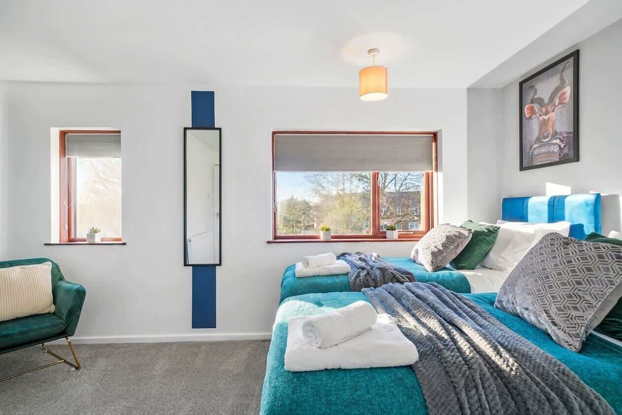 Une chambre moderne avec deux lits, un canapé vert, une grande fenêtre et un miroir.