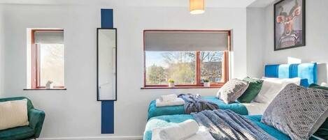 Une chambre moderne avec deux lits, un canapé vert, une grande fenêtre et un miroir.