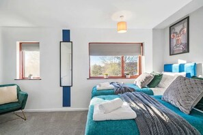 A modern bedroom with two beds, a green sofa, a large window, and a mirror. - Modern 3BED Home in Rugby - Perfect for Groups (Rugby)