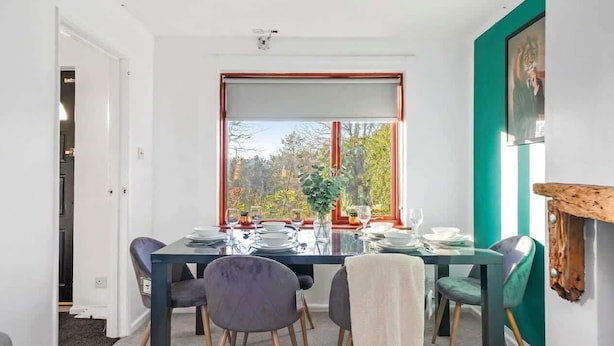 Ein Essbereich mit Tisch für vier Personen, Blick auf Bäume durch ein Fenster und ein Gemälde an der Wand.