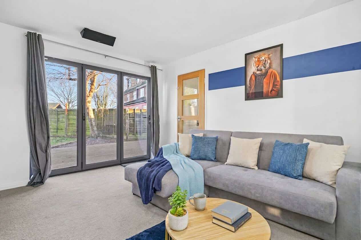 A modern living room with a grey sofa, a coffee table with books and a plant, and a large window with curtains.