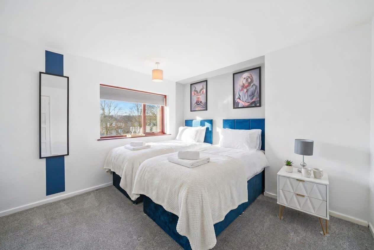 A bedroom with two beds, a bedside table, a window, and artwork on the wall.