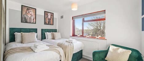 Une chambre d’hôtel avec deux lits, un fauteuil vert et une fenêtre donnant sur un beau paysage.