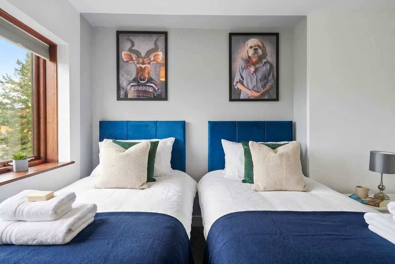 A hotel room with two beds, a large window, and artwork on the wall.