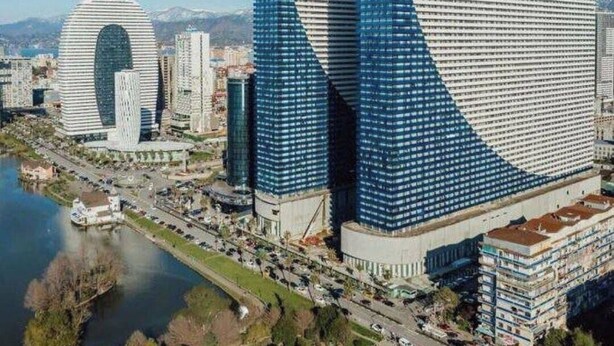 A modern cityscape with prominent skyscrapers, including a distinctive building with a large circular feature and another with a unique angular design. - Irakli GC (Batumi)