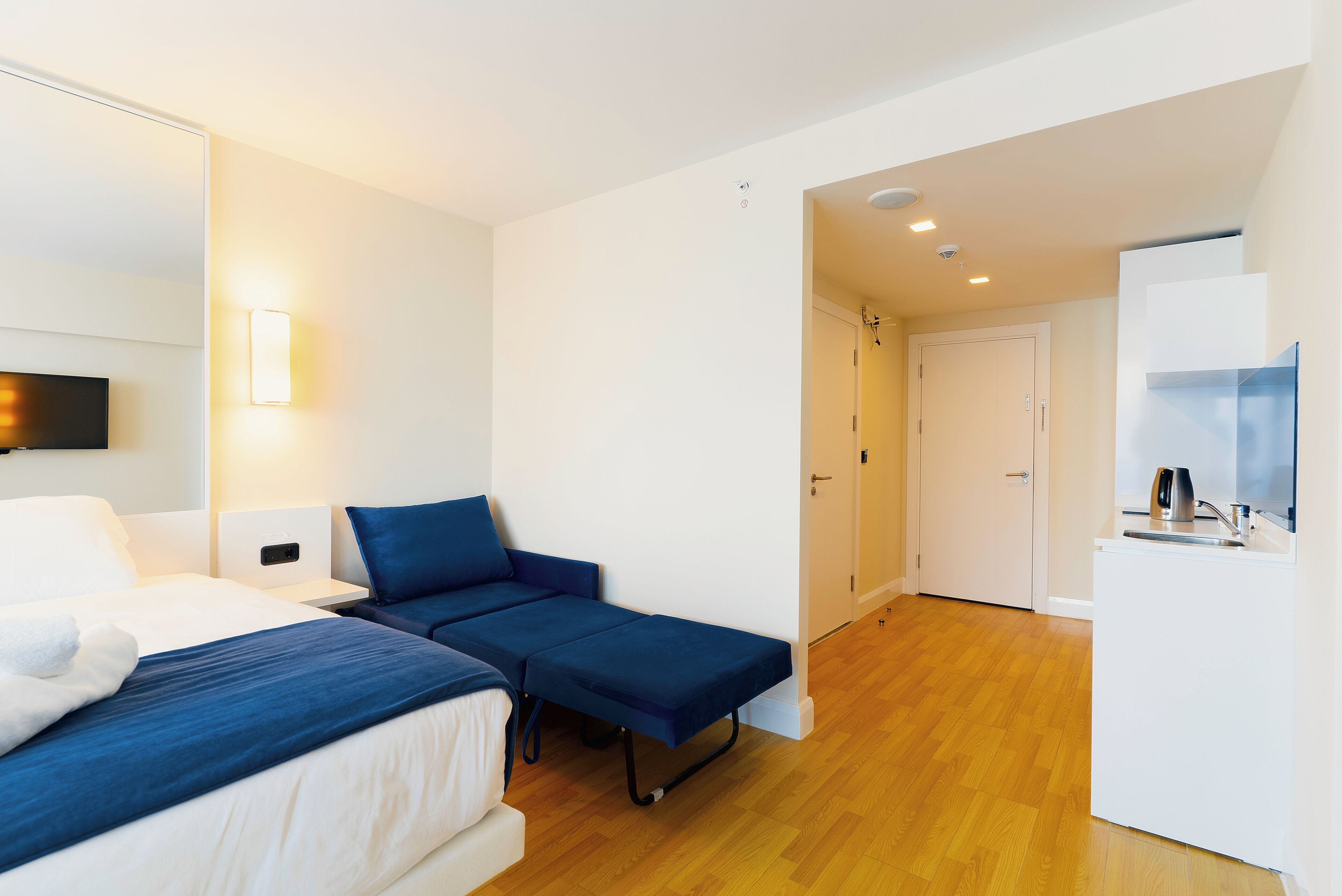 Una habitación de hotel moderna con cama, sofá cama, un escritorio pequeño y una kitchenette.