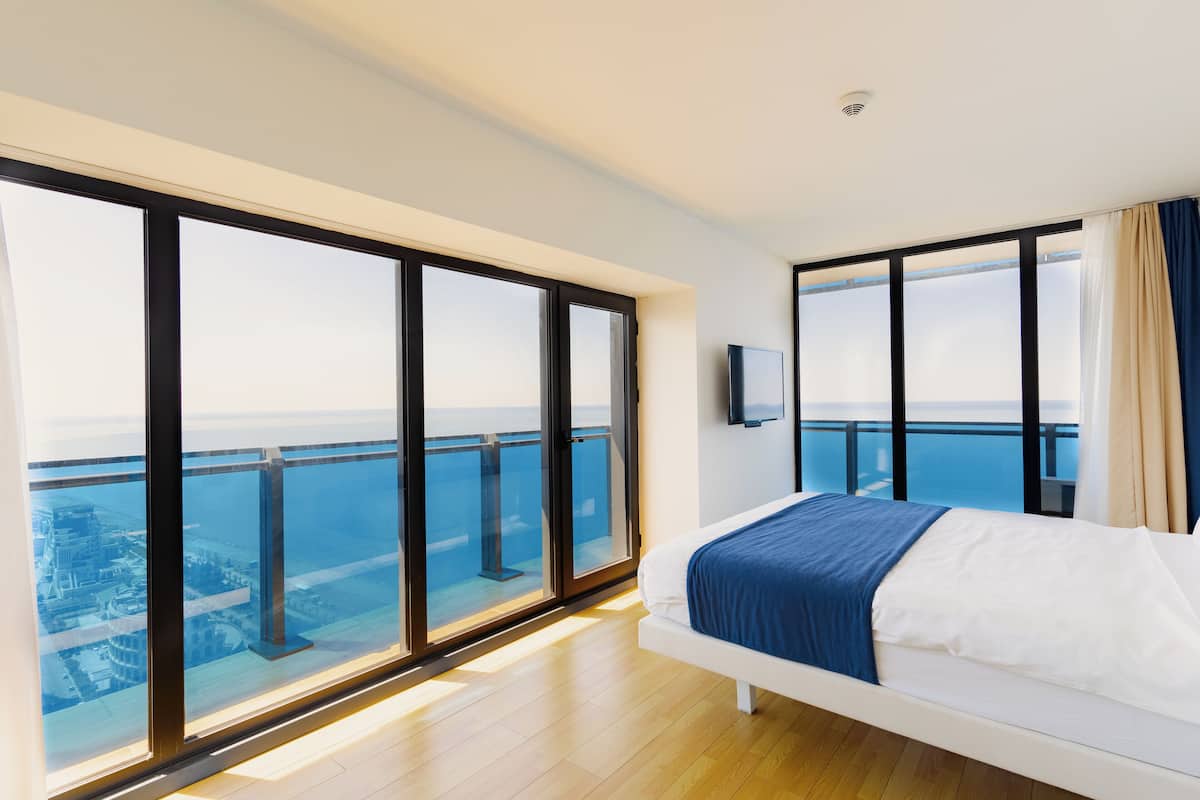 Une chambre d’hôtel moderne dotée d’un grand balcon, d’un lit recouvert d’une couverture bleue et d’un téléviseur fixé au mur.