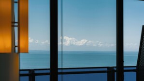A view through a window with a railing, overlooking a body of water and a distant shoreline with clouds. - Irakli GC (Batumi)