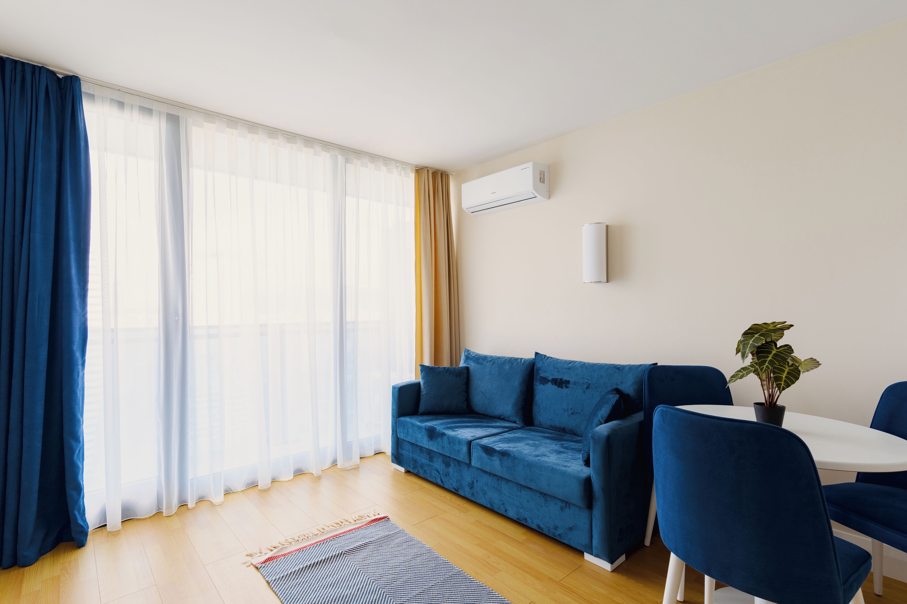 A modern living room with a blue sofa, a dining table with chairs, and a potted plant.