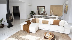 A modern living room with a white sofa, a fireplace, and a dining area with a table set for four. - My Rental Homes - Villa Floresta private pool and large garden (Sant Antoni De Portmany)