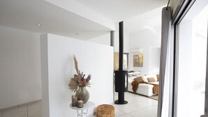 A modern interior with a white tiled floor, a small round ottoman, a white table with a vase and candles, and a black column. - My Rental Homes - Villa Floresta private pool and large garden (Sant Antoni De Portmany)