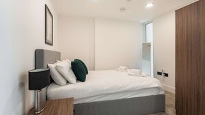 A modern bedroom with a bed, bedside table, lamp, and a framed picture on the wall. - Elegant 1BR – Sheffield City Centre (South Yorkshire)