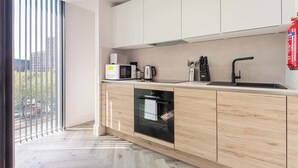 A modern kitchen with wooden cabinets, a built-in oven, a microwave, and a coffee maker. - Elegant 1BR – Sheffield City Centre (South Yorkshire)