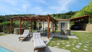 Een zwembadterras met ligbedden, een pergola en een terras van natuursteen.