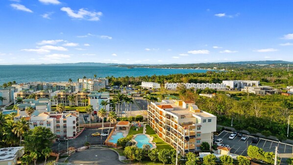 A coastal hotel with multiple buildings, a parking lot, and a swimming pool.