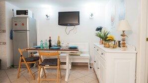 A compact kitchen with a refrigerator, microwave, and a flat-screen TV. There is a dining table with chairs, a bench, and a small cabinet with decorative items. - Amedei Apartment: 2 suites {10 m from Ponte Vecchio} (Firenze)