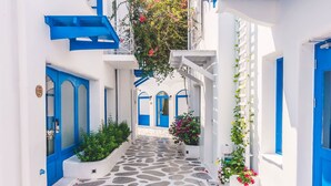 Une ruelle étroite, pavée de pierres, bordée d’immeubles blancs aux portes et fenêtres bleues.