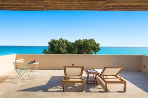 Eine Terrasse mit Meerblick, zwei Holzstühle, ein kleiner Tisch und ein Klappstuhl.