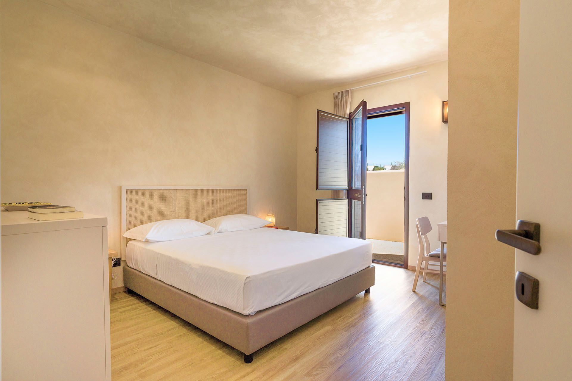 Un dormitorio con cama, mesita de noche y vistas al exterior a través de una puerta.