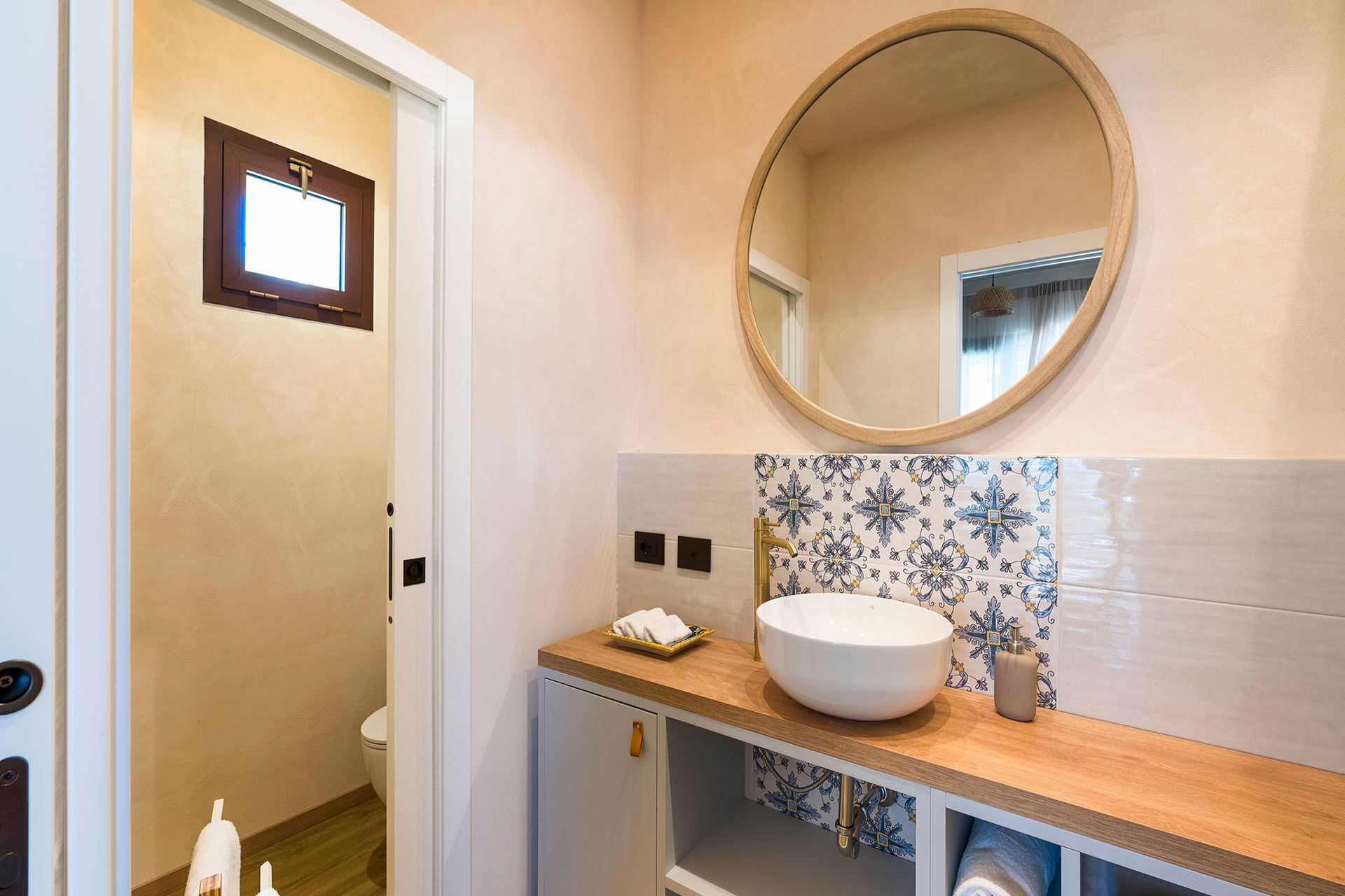 A bathroom with a round mirror, a white sink, and a patterned tile backsplash.