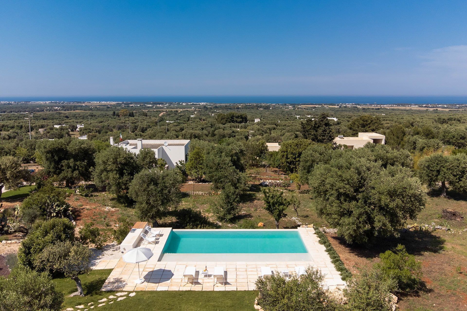 Vista aérea de una propiedad con piscina, rodeada de árboles y una lejana vista al mar.