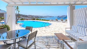 A covered outdoor area with a pool, lounge chairs, and a view of the sea. - My rental Homes | Apartment Rose 1 shared pool and air conditioning (Mykonos)