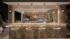 Zona de bar con pared de piedra de fondo, taburetes y una variedad de botellas y vasos.