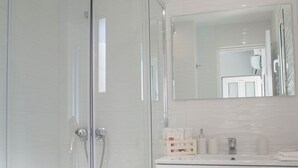 Un baño moderno con ducha de vidrio, tocador blanco con espejo y retrete.