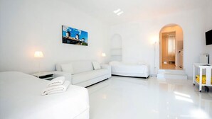 Una habitación de hotel moderna, con decoración blanca, que incluye una cama, un sofá, un cuadro de molinos y vistas a la cocina.