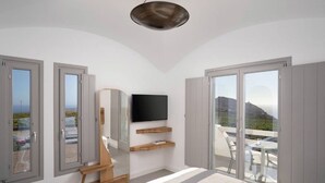 Une chambre moderne équipée d’un lit, d’une télévision, d’un miroir et d’un balcon offrant une vue sur l’océan.