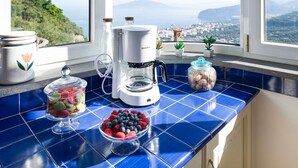 Una cocina con cafetera, un tazón de bayas y un tarro de nueces sobre una encimera de azulejos azules.