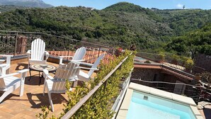 Una terraza en la azotea con mobiliario exterior, una piscina y vistas a un paisaje montañoso.