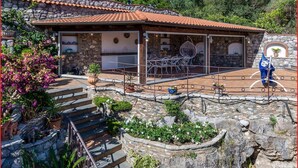 Un edificio de piedra con techo de tejas, un patio con mobiliario exterior y una escalera que lleva a la entrada.